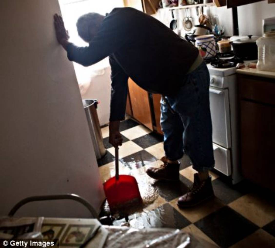Jolito Ortiz helps sweep water out of his friend's apartment while cleaning up after flooding 